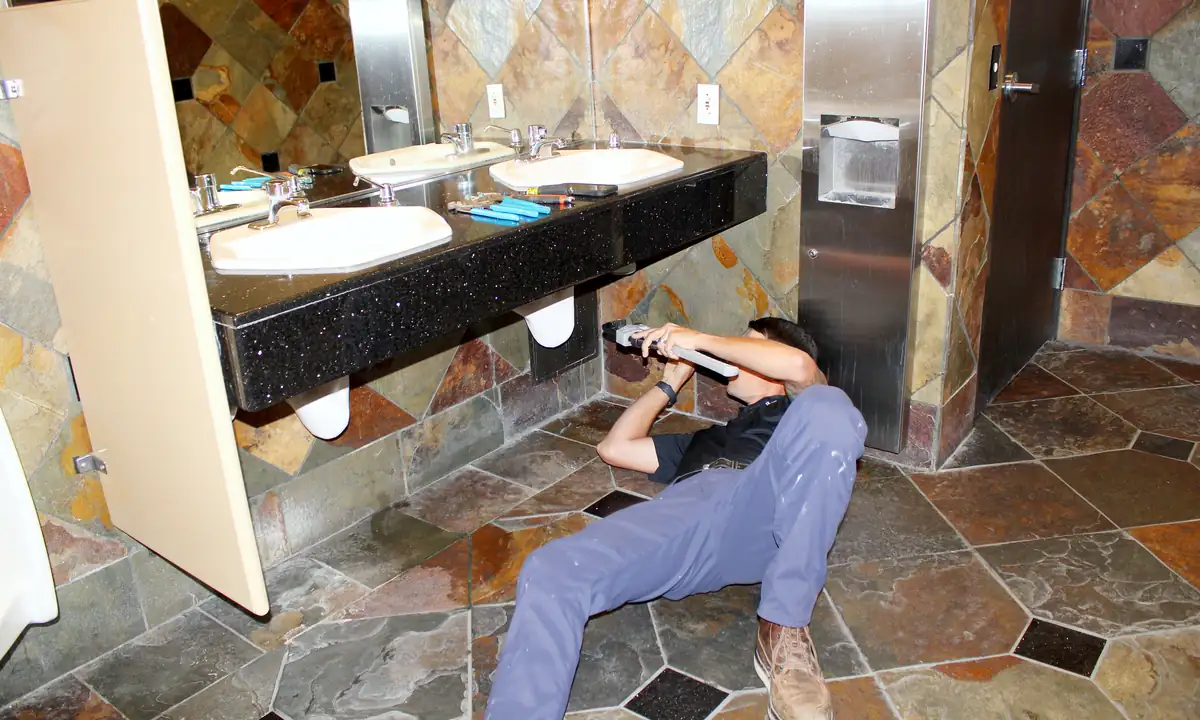 Plumber lying under a commercial restroom vanity to service sink drains and supply lines in Las Vegas
