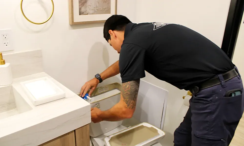 Plumber working inside a toilet tank to replace a worn fill valve
