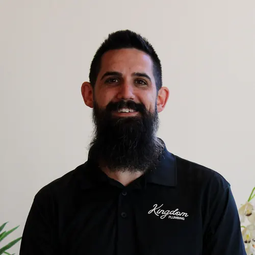 Kingdom Plumbing team member with a full dark beard in a black uniform polo