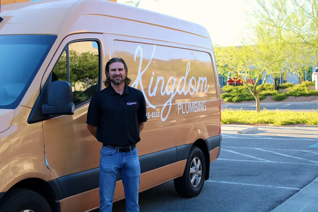 Kingdom Plumbing team member in a company polo beside a branded Kingdom Plumbing Sprinter service van in Las Vegas